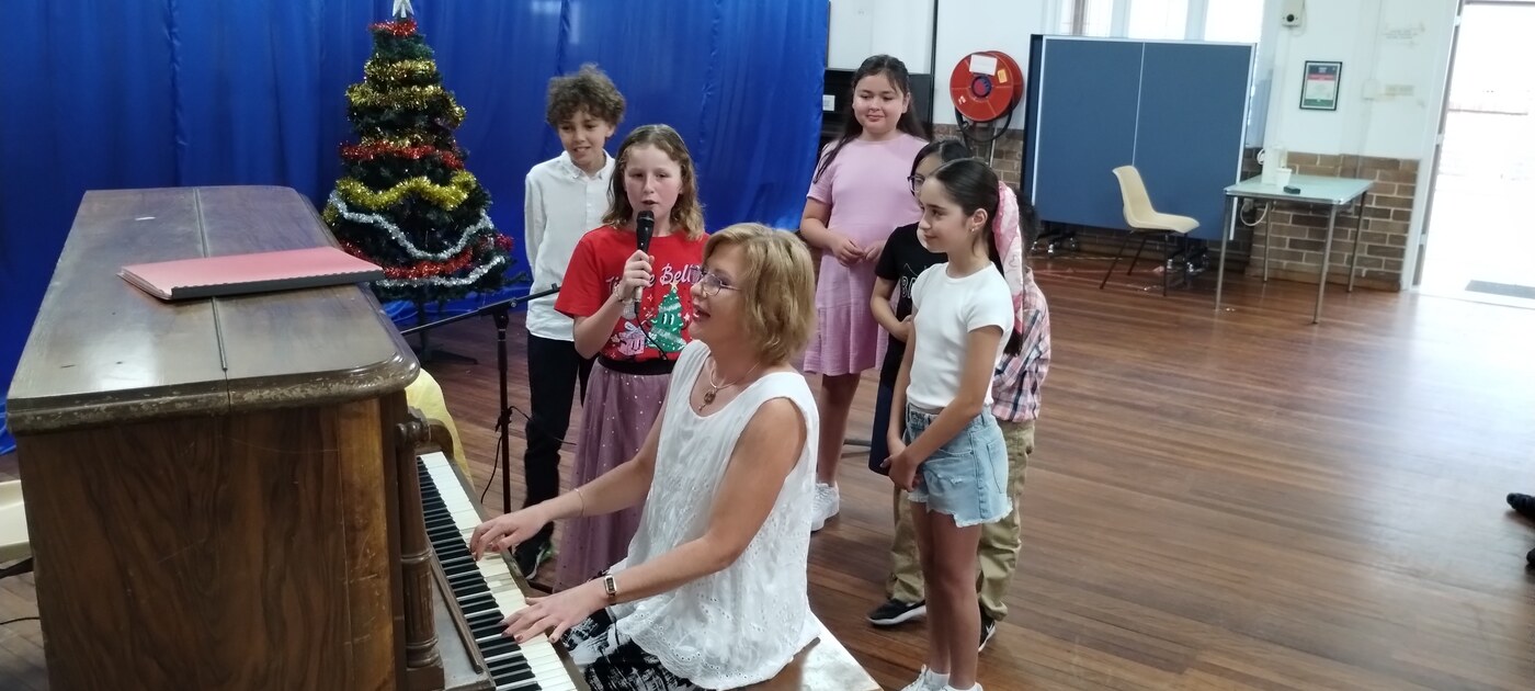 Natalie Mitz leading students in song at the piano near a Christmas tree