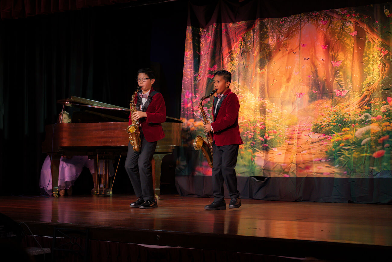 Two students playing saxophone on stage beside a grand piano