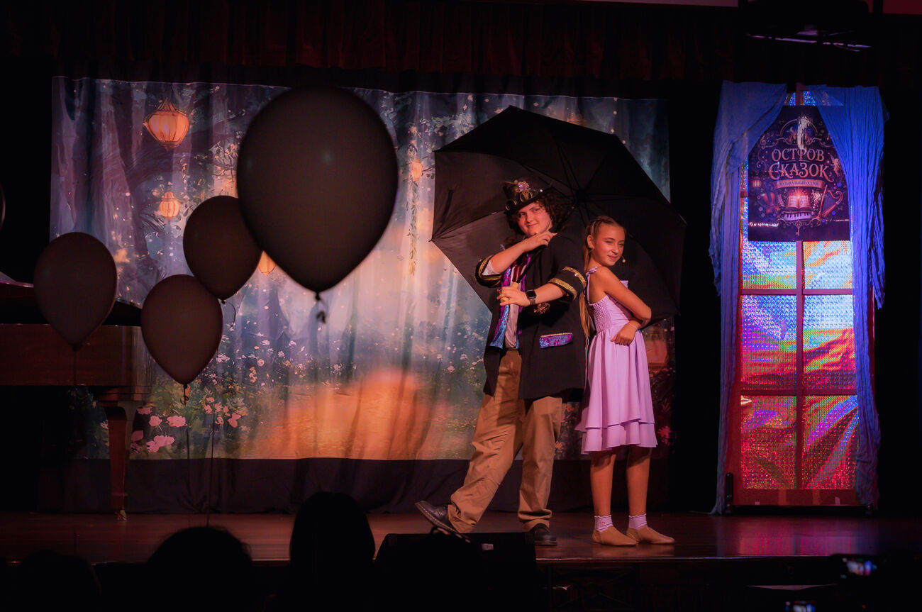 Two students posing on stage with a large umbrella prop