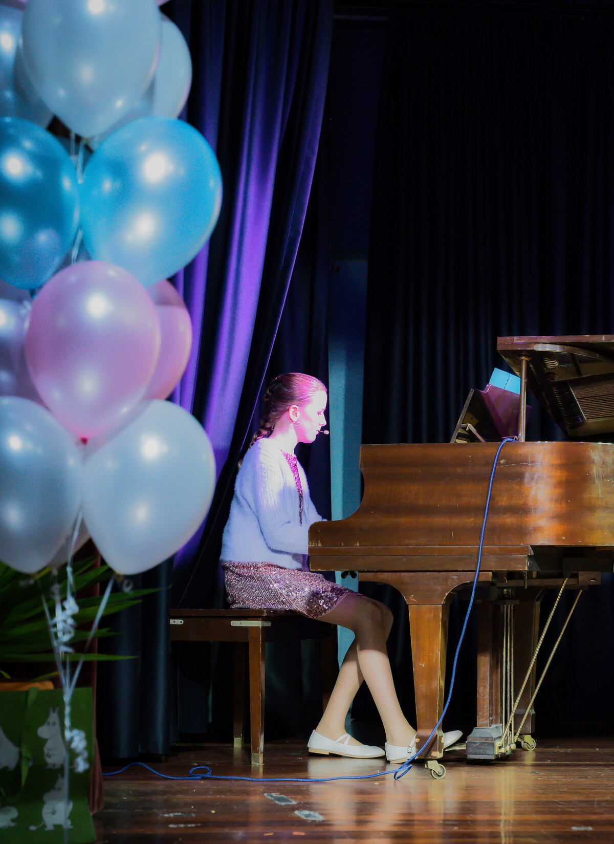 Student playing a grand piano on stage, framed by pastel balloon decorations